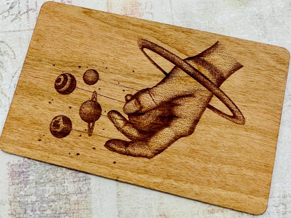 Engraved wooden card showing a hand holding the solar system
